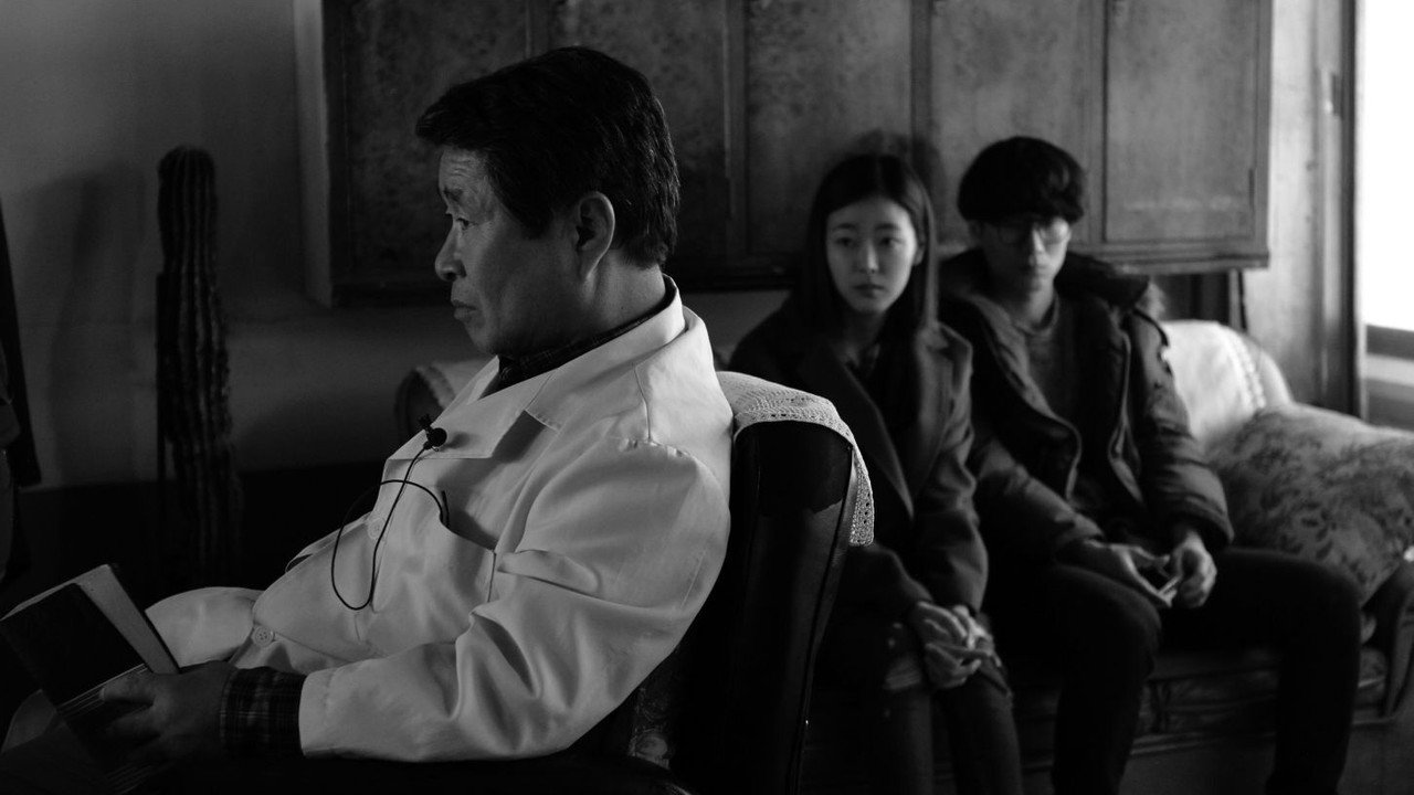 실내 앞쪽의 중년 남성 뒤로 젊은 두 사람이 소파에 앉아 있다