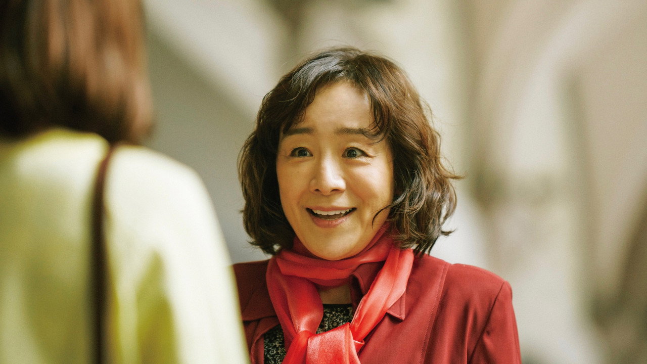 붉은 옷과 목도리를 두른 여성이 앞에 선 사람을 보며 웃는다