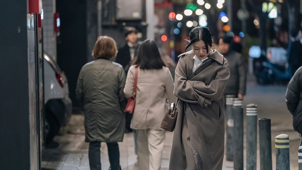 밤의 보행자 거리에서 코트를 여미고 걸어가는 여성