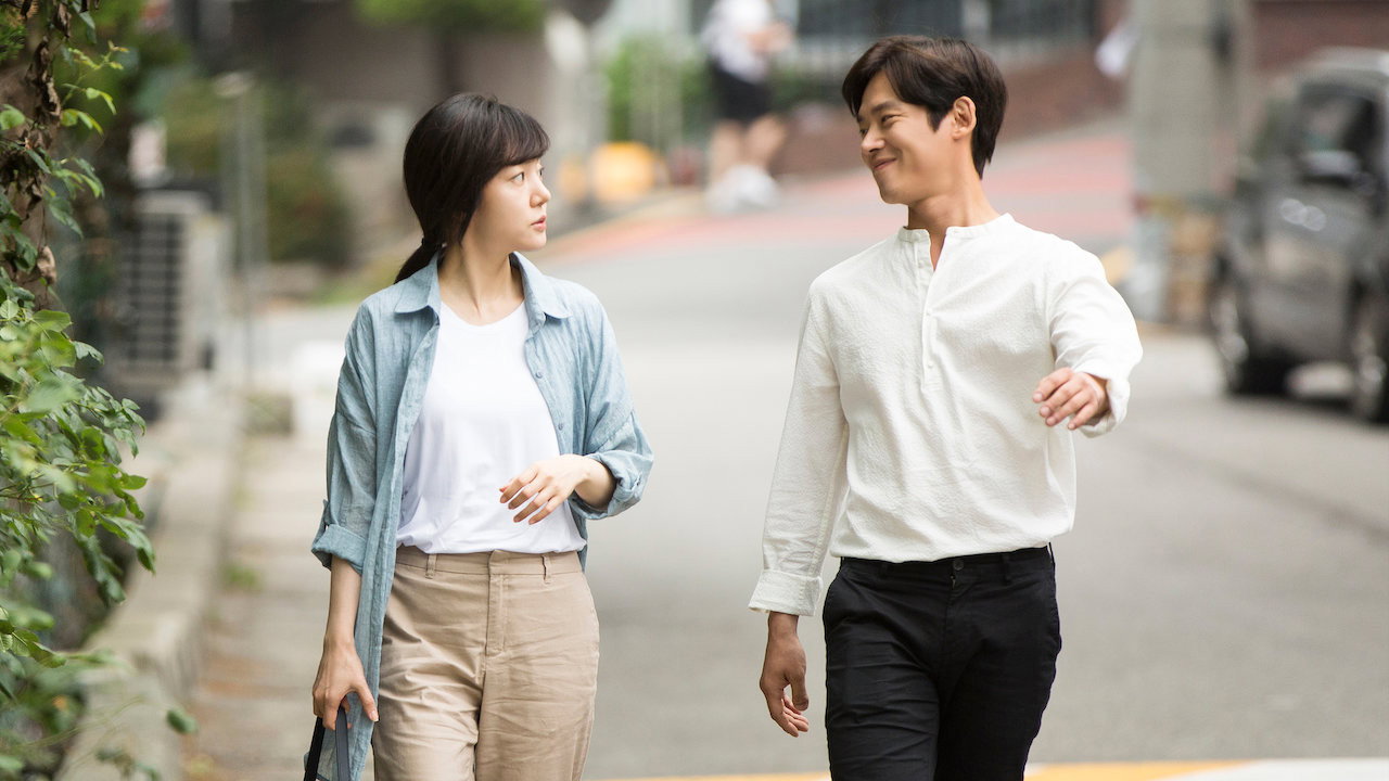 낮의 주택가 골목에서 두 사람이 서로를 보며 나란히 걷는다