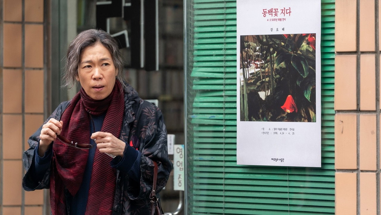 녹색 덧문과 그림 안내가 붙은 건물 앞에 여성이 서 있다